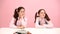 Happy little twin schoolgirls sitting behind school desk. Frontal view. Over pink