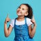 Happy, looking and a child pointing in a direction isolated on a blue background in a studio. Smile, thinking and a