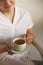 Happy lovely young female health worker laughing sincerely while holding cup of hot tea