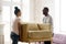 Happy loving african spouses carrying new armchair to living room