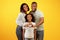 Happy loving family. Black parents holding hands in heart shape sign, posing with liitle daughter over yellow background