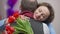 Happy loving woman hugging adorable man holding bouquet of flowers smiling and looking at camera. Portrait of beautiful