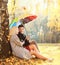 Happy loving young couple sitting under tree with colorful umbrella in sunny day falling leaves