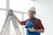 Happy male builder standing on ladder with screwdriver infront of window.