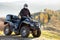Happy male driver in protective helmet enjoying extreme ride on atv quad motorbike in autumn mountains at sunset