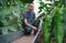 Happy male farmer hoed soil on bed of vegetables inside greenhouse. Smiling gardener near cucumber and pepper vegetable bed.