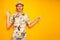 happy male tourist traveler in Hawaiian shirt hat isolated on yellow background points with his finger at an empty