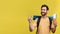 Happy man with backpack holding passport with tickets and pointing aside at free space, yellow background, panorama