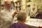 Happy man cutting senior customer\'s hair with razor