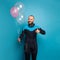 Happy man in diver suit holding birthday balloons and showing thumb up against vivid blue studio wall background
