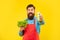 Happy man giving juice bottle holding fresh lettuce yellow background, juice barkeeper