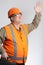 Happy man in hard hat and reflective vest waving hand on grey background, builder with tool in case greeting partners