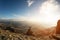 A happy man with his hands up high stands on top of a separately standing rock that is above the clouds against the