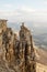 A happy man with his hands up high stands on top of a separately standing rock that is above the clouds against the