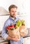 Happy man holding paper grocery shopping bag in the kitchen