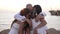 Happy man hugging wife and daughters standing at sunset on Mediterranean sea shore in sunbeam. Loving Caucasian father