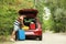 Happy man packing suitcases into car trunk near forest