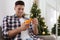 Happy man peeling tangerine near Christmas tree indoors