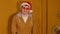 Happy man in santa hat and fashionable glasses expresses positive and festive emotions on brown background. Stylish male