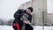 Happy man stroking fluffy dog on winter walk on snowy city landscape. Cheerful dog owner scratching happy puppy on snowy