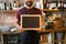 Happy man or waiter with blank blackboard at bar