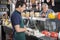 Happy Man Watching Worker Slicing Cheese In Shop