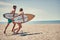 Happy man and woman surfers running together to surf at the beach .