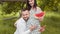 Happy married couple with watermelon in hands posing at green garden. Handsome man embracing pregnant wife. Family and