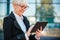 Happy mature businesswoman standing in front of an office building and browsing internet on a tablet