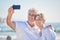 A happy mature caucasian couple enjoying fresh air on vacation at the beach while using a cellphone. Smiling retired