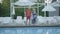 Happy mature couple standing at the swimming pool hugging their little granddaughter. Grandmother and grandfather