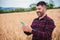 Happy mature farmer using cellphone device on a harvest wheat. Caucasian cowboy browsing on internet using a mobile