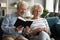 Happy mature husband reading book while smiling elderly wife knitting.