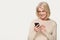Happy mature senior woman using smartphone isolated on grey background