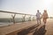 Happy mature woman and man walk joining hands along footbridge in summer evening