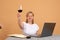 Happy mature woman using laptop computer and drinking wine, shows cheers sign