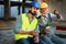 Happy mature and young engineer, architect, worker sitting at building site and resting