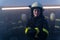 Happy mid adult female firefighter looking at camera indoors in fire station at night.