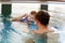 Happy middle-aged father swimming with cute adorable baby girl in swimming pool.