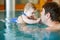 Happy middle-aged father swimming with cute adorable baby girl in swimming pool.