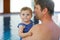 Happy middle-aged father swimming with cute adorable baby girl in swimming pool.