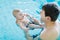 Happy middle-aged father swimming with cute adorable baby in swimming pool. Smiling dad and little child, newborn girl