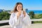 Happy middle-aged female in white bathrobe on balcony of hotel in seaside resort town