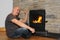 Happy middle aged man sitting near a hot burning fireplace, winter relaxation concept