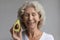 Happy middle aged retired lady holding slice of ripe avocado.