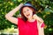 Happy middle-aged woman in red shirt and blue hat holding ice-cream in waffle cone like microphone and laughing outdoors