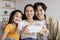 Happy millennial attractive japanese man, woman and teenager girl making photo together on smartphone