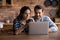 Happy millennial couple using laptop in kitchen, watching show together