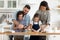 Happy millennial married couple teaching small kids making homemade pastry.