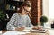 Happy millennial woman taking notes in notepad while working at laptop in comfortable loft office